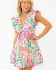 Close-up of Meet Me in Santorini Aegean Garden Dress highlighting flutter sleeves, deep neckline, and vibrant pink waist tie.