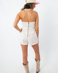 Back view of model in white denim romper with zipper closure and beige cowboy boots
