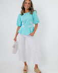 Model wearing retro daisy aqua blouse with white pants