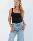 RD Style Scoop Bodysuit Black features a sleek sleeveless design with a scoop neckline, styled with light-wash jeans for a chic layered look.