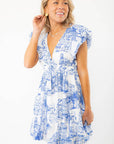 Model wearing the Meet Me in Santorini Dress with flutter sleeves and Mediterranean print, styled for a summer getaway look.