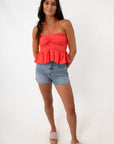 Woman wearing coral eyelet halter top with denim shorts, front view