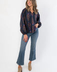 Full-body view of At Long Last Navy Long Sleeve Blouse featuring floral balloon sleeves and tassel ties, paired with jeans and heeled mules.