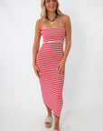 Woman in red and white striped strapless knit midi dress with side slit, wearing beige platform sandals and a blue necklace, standing against white background