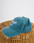Teal Pawleys Island cap displayed on a wicker surface