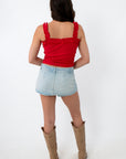 Person wearing a red top and light blue denim skirt with beige boots on a white background