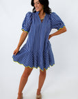 Side view of woman in blue striped dress with yellow trim, smiling, looking down