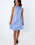 Woman in blue pinstripe dress with ruffled neckline and bow detail, standing against white background