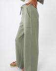 Woman in sage green lounge pants and white top, smiling and posing sideways