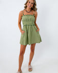 Woman in green striped mini dress with beaded straps, smiling, standing against white background