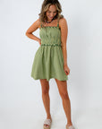 Side view of woman in green striped dress with beaded straps, smiling, white background