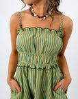 Close-up of woman’s face and beaded necklace, wearing green striped dress with ruffled top