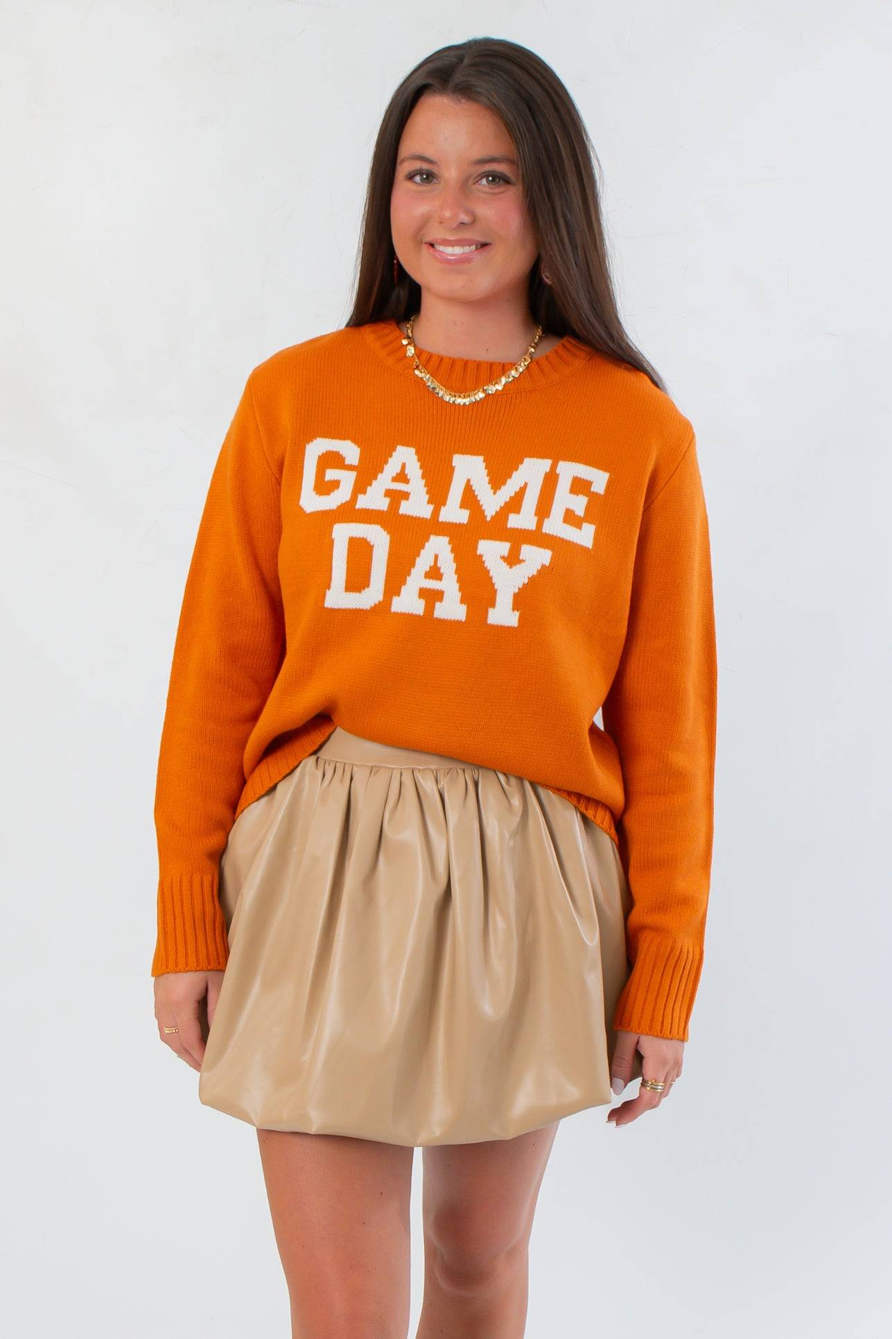 Game Day Orange Knit Sweater with bold white block letters, styled with a beige skirt for a cozy fall game day look.