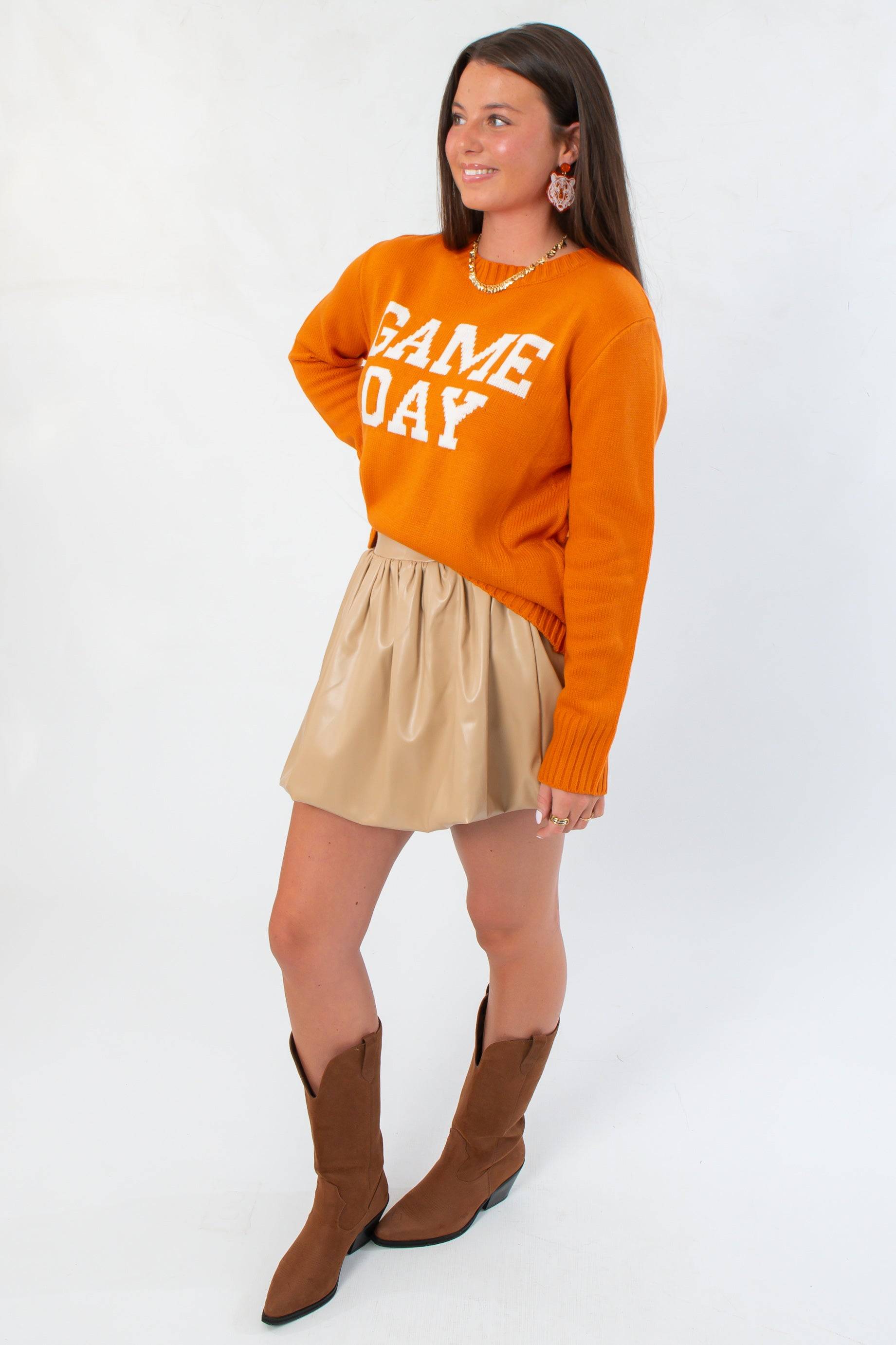 Side view of Game Day Orange Knit Sweater styled with a pleated beige skirt and western boots, ideal for fall gameday outfits.