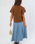 Back view of light brown V Neck Sweater Vest with ribbed hem, worn with a flowy blue skirt and brown platform boots.