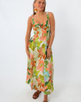 Woman in tropical floral maxi dress with colorful earrings and brown sandals