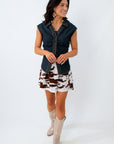 Woman wearing a denim vest over a patterned dress with beige boots on a white background