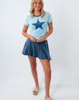 Woman wearing a light blue t-shirt with a star design and a denim skirt on a white background