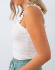 Woman wearing a white sleeveless top with ruffled details on a plain background
