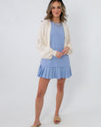 Woman in blue pleated hem mini dress with cream cardigan, sunglasses, and gold jewelry