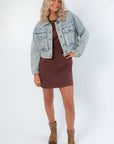 Maci Medium Wash Crop Denim Jacket – Classic & Trendy trucker jacket paired with a brown mini dress and ankle boots for a fall-ready look.