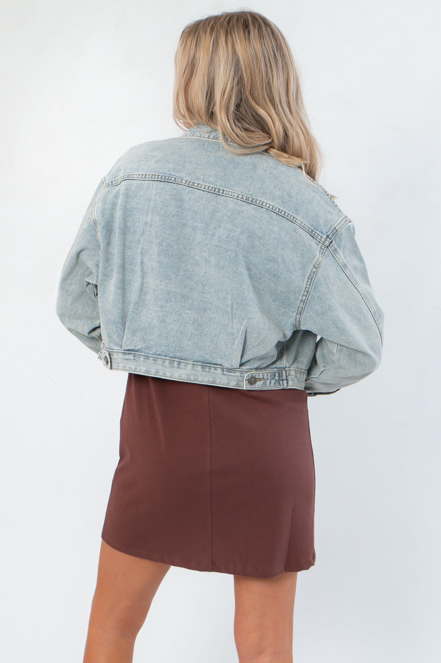 Back view of Maci Medium Wash Crop Denim Jacket – Classic & Trendy, highlighting adjustable waist tabs and faded denim texture.