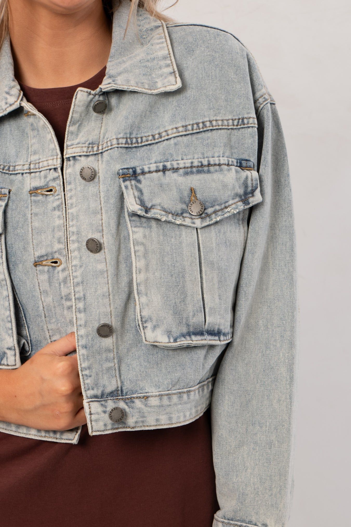 Close-up of Maci Medium Wash Crop Denim Jacket – Classic & Trendy, featuring distressed flap pockets and metal button detailing.