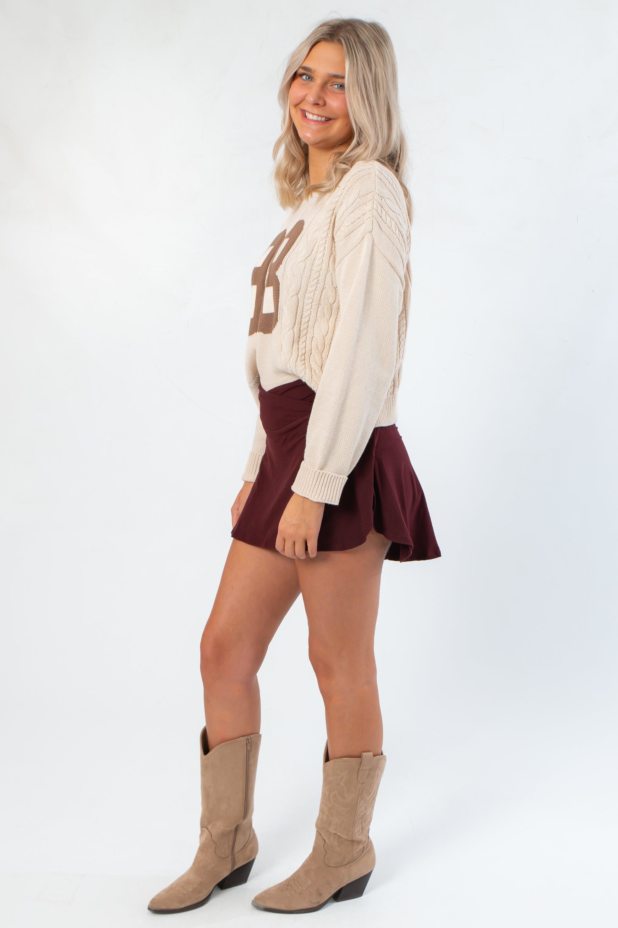 Side view of Dark Cherry Yoga Skort featuring flared hem and crossover waistband, paired with neutral sweater and boots for a gameday look.
