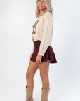 Side view of Dark Cherry Yoga Skort featuring flared hem and crossover waistband, paired with neutral sweater and boots for a gameday look.