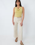 Model wearing yellow sleeveless cowl neck top with cream wide-leg pants and sandals