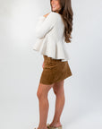 Side view of Effortless Icon Ivory Peplum Cardigan – soft ivory knit cardigan with flared hem, paired with a brown suede skirt and heeled sandals.