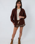Women’s brown button-up shirt with long sleeves, layered over a white top, paired with embroidered shorts and cowboy boots