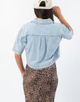 Back view of Delilah Denim Short Sleeve Woven Top highlighting pleated detail and relaxed fit, a must-have denim shirt for fall layering.