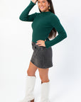 Side profile of Taylor Emerald Green Ribbed Long Sleeve Top showcasing its slim fit and textured knit, paired with a casual skirt and boots.