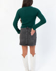 Back view of Taylor Emerald Green Ribbed Long Sleeve Top highlighting ribbed texture and snug fit, styled with a black denim skirt.