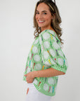 Side profile of women wearing green gingham sequin golf tee blouse with white pants