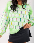 Close-up of Queen of Sparkles Green Golf Ball & Tee Sweatshirt showing glittery sequin golf balls and multicolor tees on green fabric.
