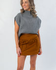 Amber Chai Sienna Twill Mini Skirt featuring front bow details, styled with a sleeveless gray sweater for a trendy seasonal outfit.
