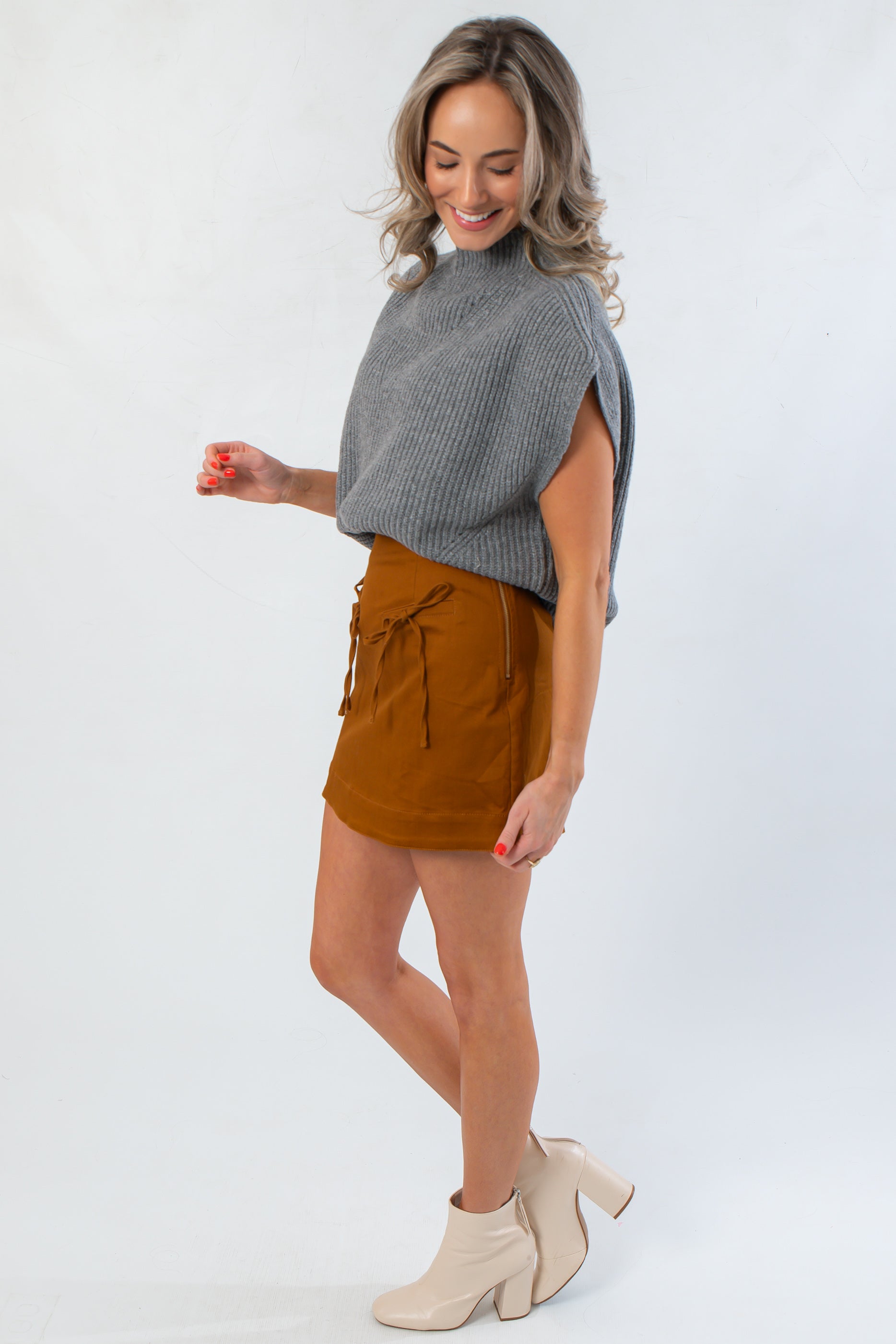 Amber Chai Sienna Twill Mini Skirt with bow accents styled for fall, paired with a cozy gray top and cream heeled boots for a modern look.