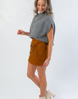 Amber Chai Sienna Twill Mini Skirt with bow accents styled for fall, paired with a cozy gray top and cream heeled boots for a modern look.