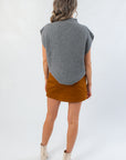 Woman wearing a gray sleeveless sweater over a brown skirt on a white background