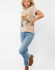 Full-body shot of a model wearing the Daydreamer Willie Nelson 'A Horse Called Music' Graphic Tee with blue jeans and brown boots.