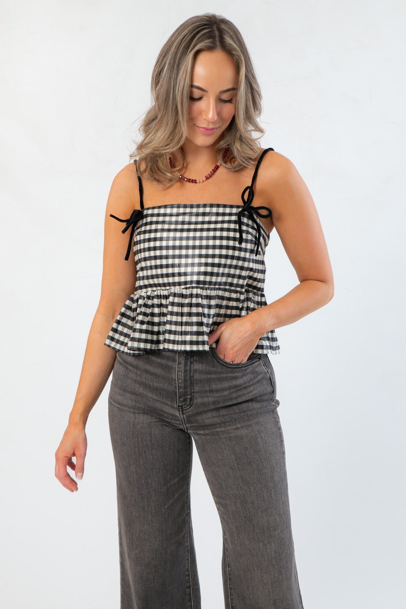 Girly Girl Shiny Black Gingham Peplum Top – Cute & Chic tank top with velvet bows and adjustable straps, styled with wide-leg jeans.