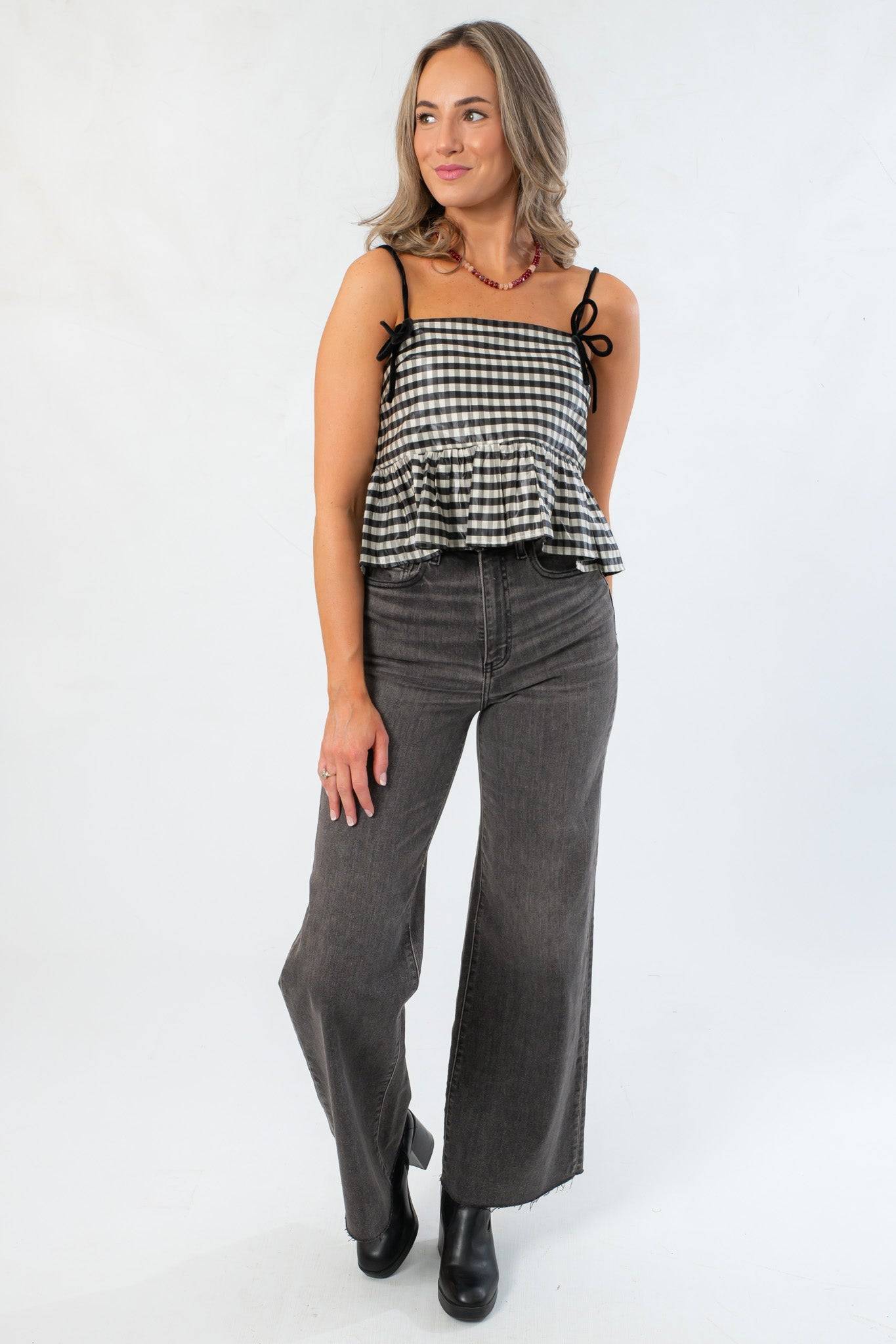 Full front view of Girly Girl Shiny Black Gingham Peplum Top paired with high-waisted gray jeans and black boots for a trendy look.
