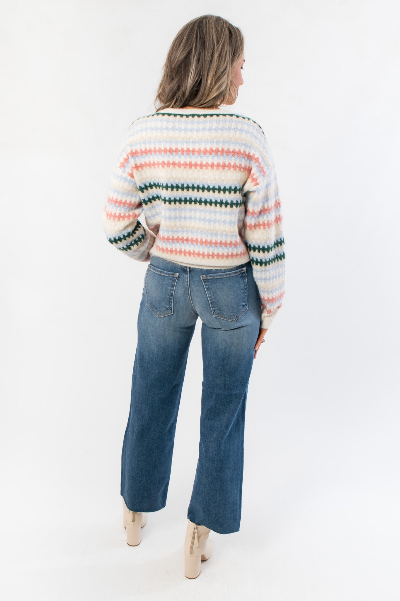 Back view of Mountain Top Stripe Knit Sweater with multi color stripe design and ribbed hem, paired with high-waisted denim jeans.