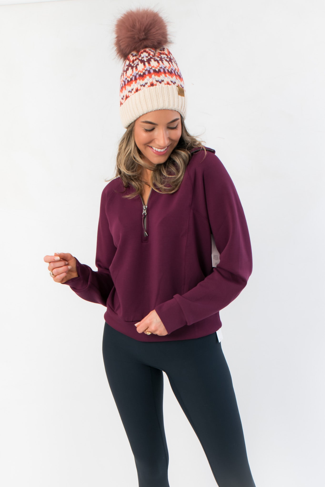 Spanx Plum Berry Air Essentials Half Zip Sweatshirt for women in a rich plum color, styled with black leggings and a knit beanie.