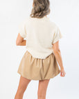 Back view of Football Bow Mock Neck Cream Sweater with ribbed hem and mock neckline, styled with a tan mini skirt for gameday fashion.