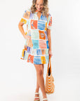 Model wearing THML At Sea Nautical Printed Dress with beach-themed prints and pockets, styled with a straw tote for a casual summer look.