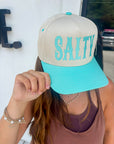 Person wearing a beige and turquoise cap with 'SALTY' text.