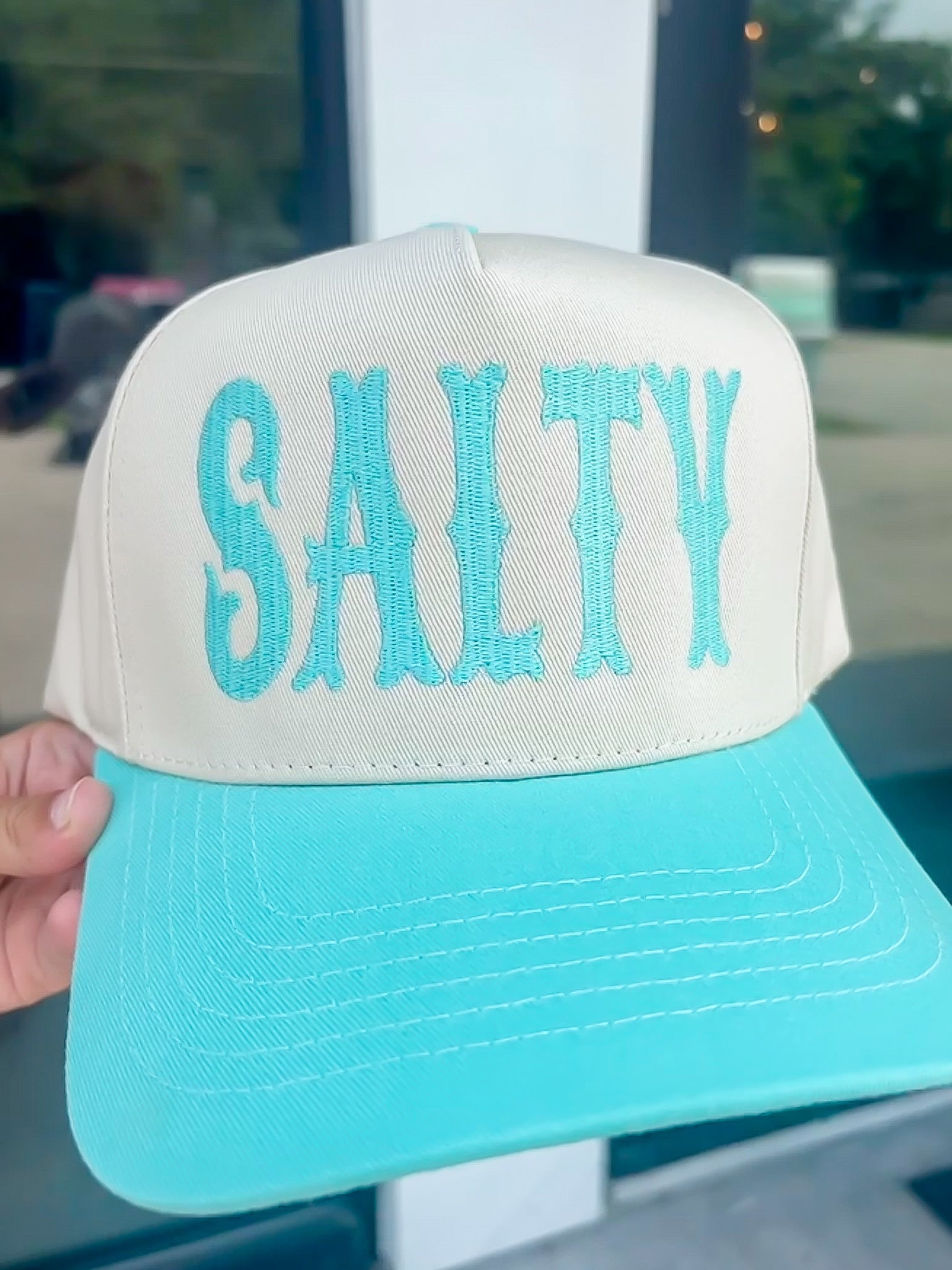 Trucker hat with 'SALTY' in turquoise on a white background
